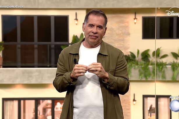 Leandro Hassum de blusa branca e casaco verde, gesticulando, no glass de estúdio da Casa do Patrão